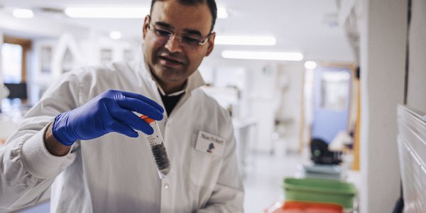 

En mannlig forsker i hvit frakk er på et laboratorie. I hånden holder han et rør med en sedimentprøve