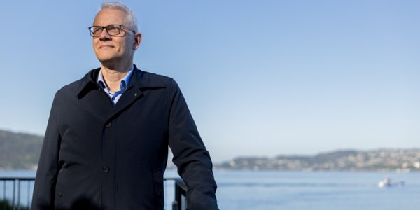 

en mann i frakk med blått hav bak seg 