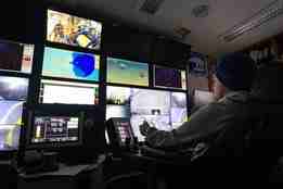 En mann sitter i et kontrollrom med mange skjermer og styrer undervannsroboten.