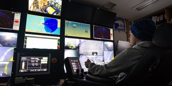 

En mann sitter i et kontrollrom med mange skjermer og styrer undervannsroboten.