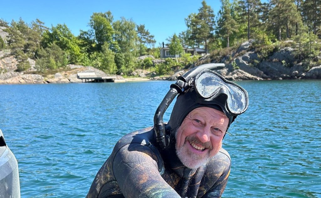 Foto av en blid havforsker Stein Mortensen med sjø, svaberg og skog i bakgrunnen