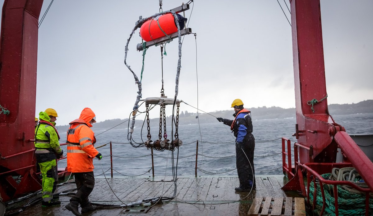 Forskere i arbeidstøy på båt senker utstyr i fjorden.