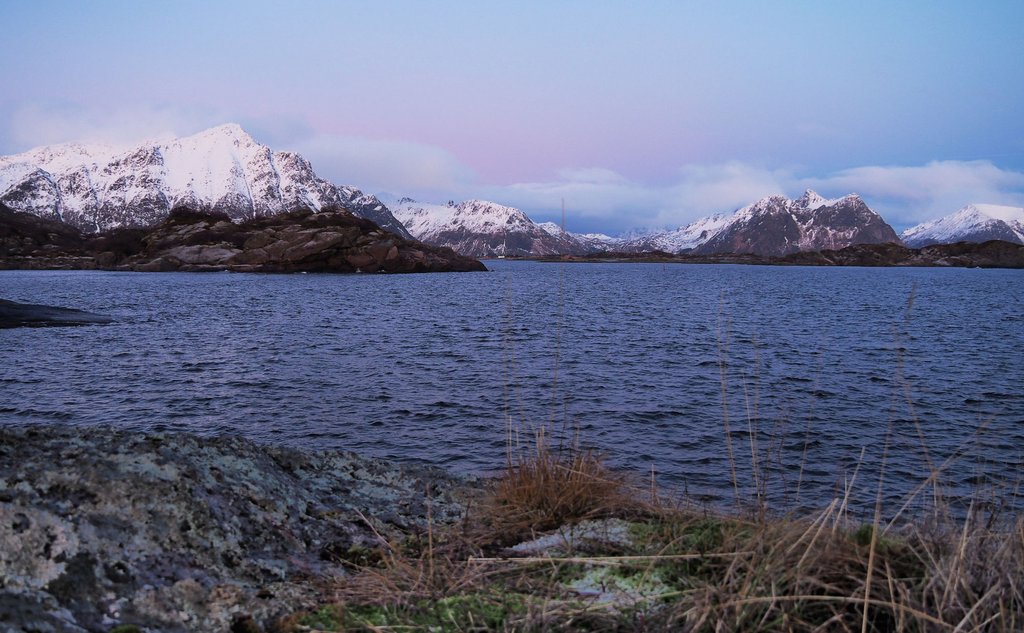 Foto av fjor og snødekte fjell, himmel med kveldslys farga i blåtoner.