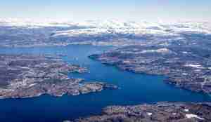 Flybilde av fjord med snø på fjelltoppene i bakgrunnen.