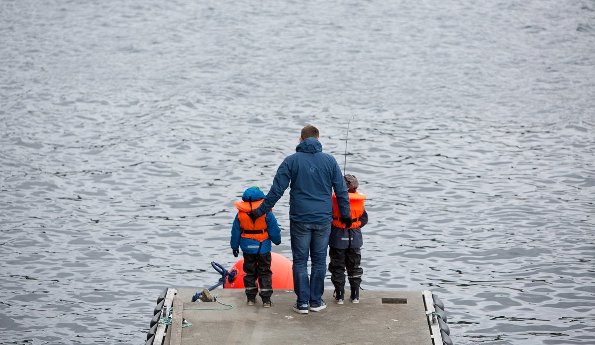 
Mann og to barn står med ryggen til kamera på en brygge og fisker.