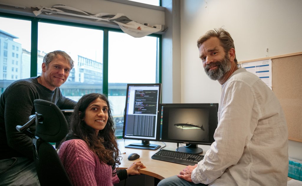 Three scientists in front of a computer, smiling to the camera.