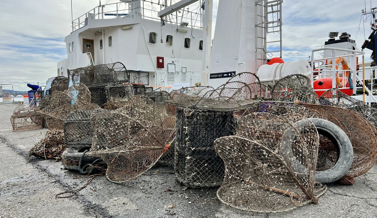 
Stabel av opphentede spøkelsesteiner på kaia med båt bak