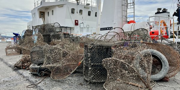 

Stabel av opphentede spøkelsesteiner på kaia med båt bak