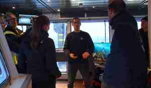 foto av person på broen til båt som forteller om noe til et lite publikum