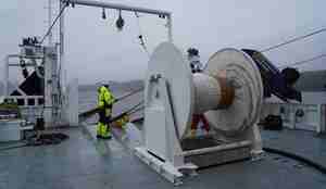 foto av mann på dekket til en båt, foran en trommel