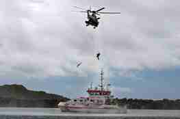 Rescue helicopter with an operator on the winch, extracting a person from a boat.