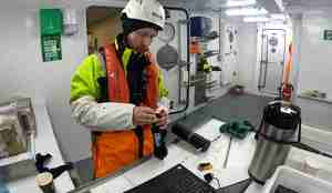 Tekniker Eirik Bygdnes er klar til å laste ned data fra en av lyttebøyene. Han står inne i båten, foran en pc, med bøyen i hendene.