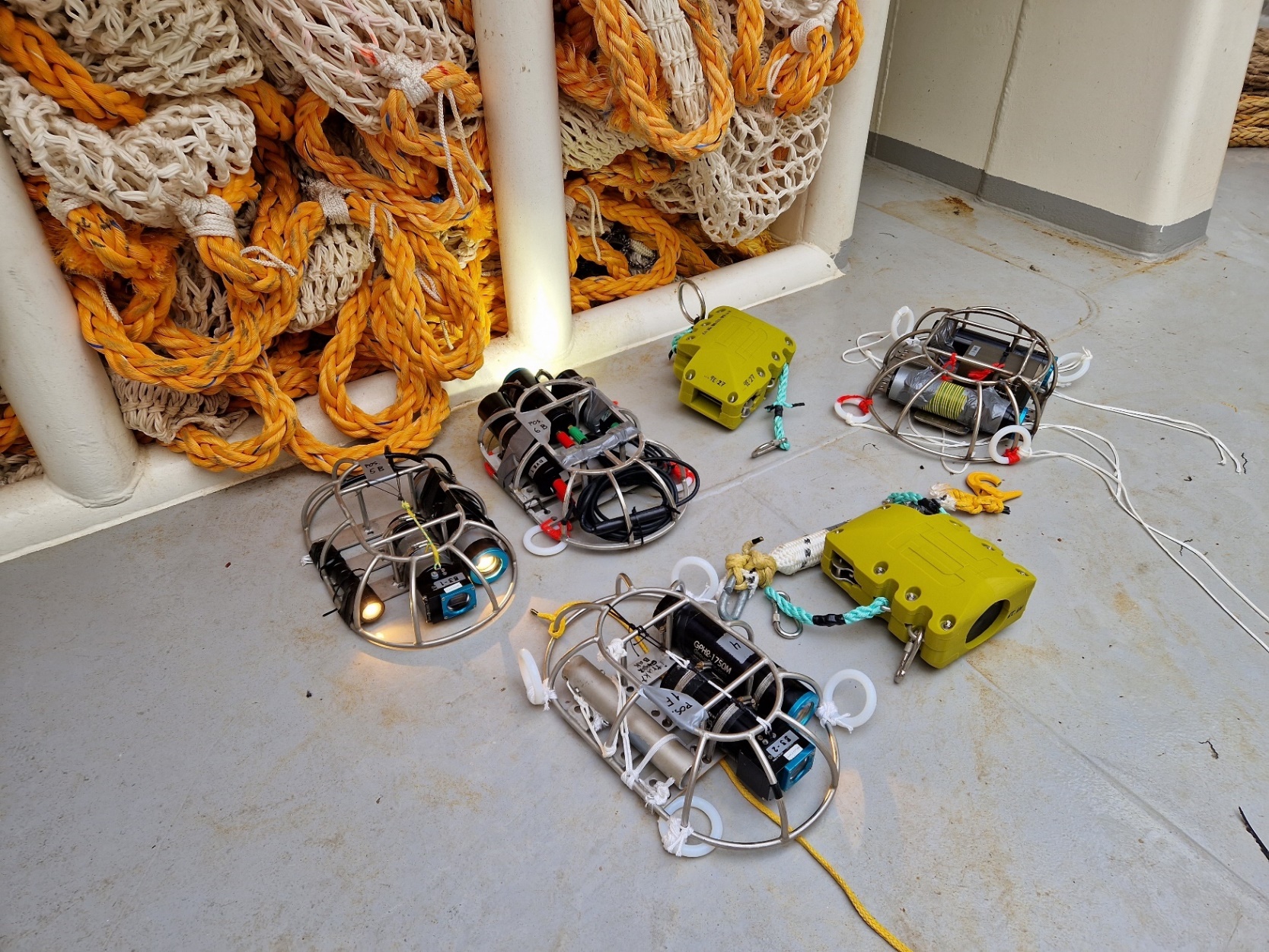 Figure A1 – various camera systems and other instruments ready for deployment before Test haul #T2: top left, GoPro cameras (in a B-group housing) in a protective steel “dome-frame”, with two white lights; top centre a FossTech Codend Choker Unit (CCU); top right, the “DarkVision” camera system in a “dome-frame”; centre right, a removal depth sensor and backup CCU; and bottom centre, a GoPro Hero 5 (in a B-group housing) in a “dome-frame”, with one white light and a depth sensor, for monitoring the CCU opening time and depth.  