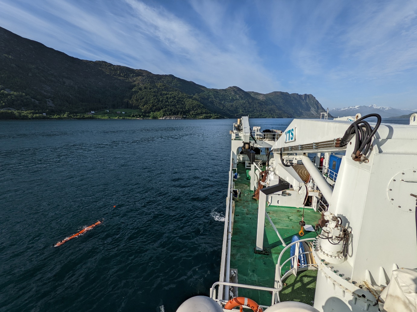 Photo taken from high on the ship showing the rear of the ship, the AUV in the water and the terrain of Rovdefjorden