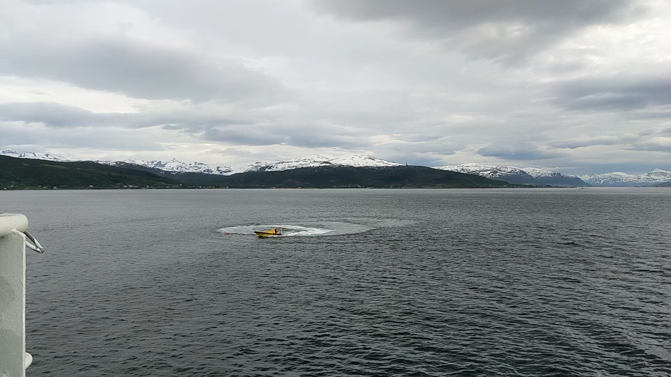 Photo of Man Overboard Boat (MOB) doing circles around the AUV at the test site wtih mountains behind