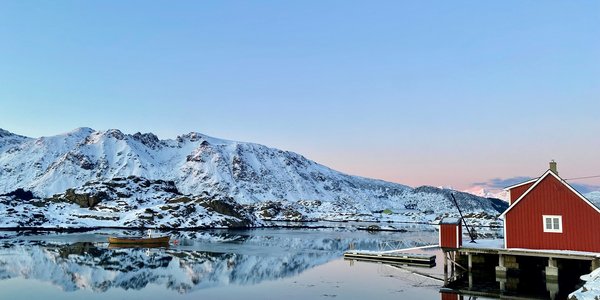 

Rødt naust ved havet, båt ligger på blikkstille vann med lave fjell i bakgrunnen. 