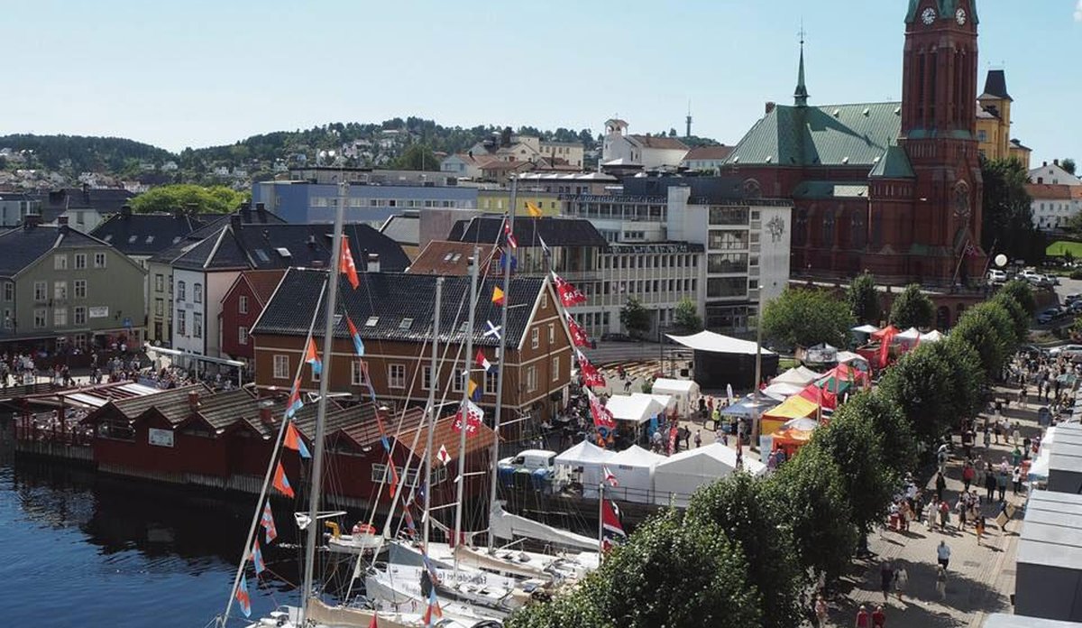 
Promenade med flotte seilbåter med norske flagg, trær og sol 