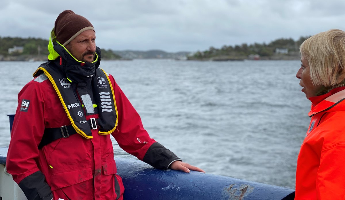 To personer i regntøy snakker sammen i en liten båt.