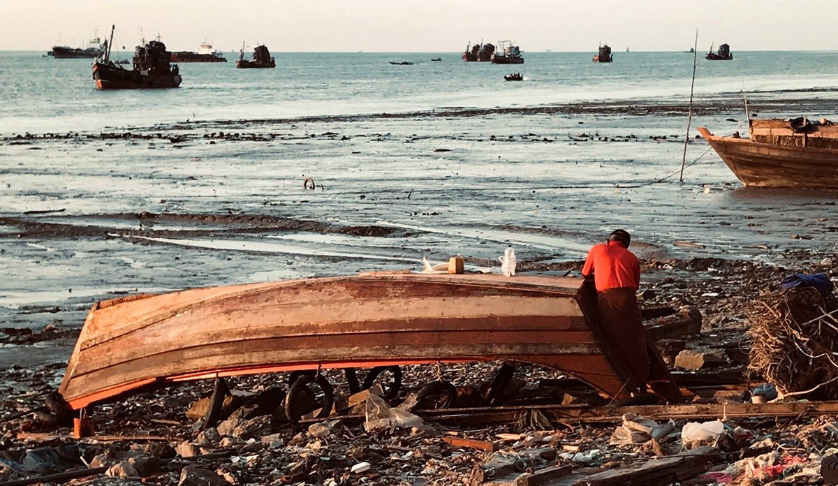 
Båt på strand, flere fiskebåtar på sjøen.