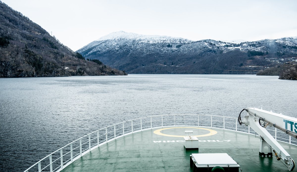 
Forskingsfartøy i fjord, fjell i bakgrunnen.