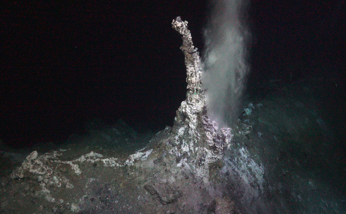 Noe som kan minne om en lang skorstein som smalner mot toppen stikker opp fra havbunnen som består av samme materiale.