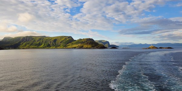 Bilde tatt fra båt med sjø, fjell og øyer i bakgrunnen.