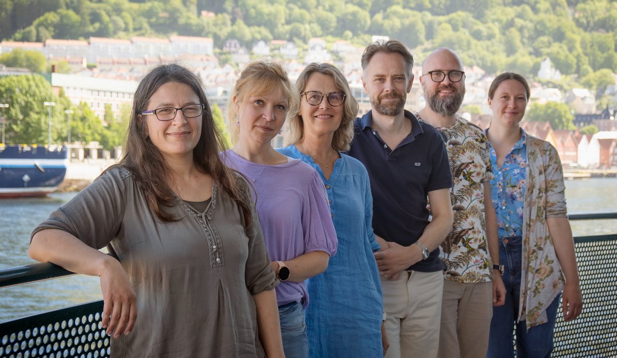 
Seks forskarar står ute på ein veranda, med Vågen og Bryggen i Bergen i bakgrunnen.